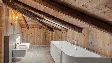 Une salle de bain avec un sol en pierre, une baignoire sur pieds et un lavabo fixé au mur.