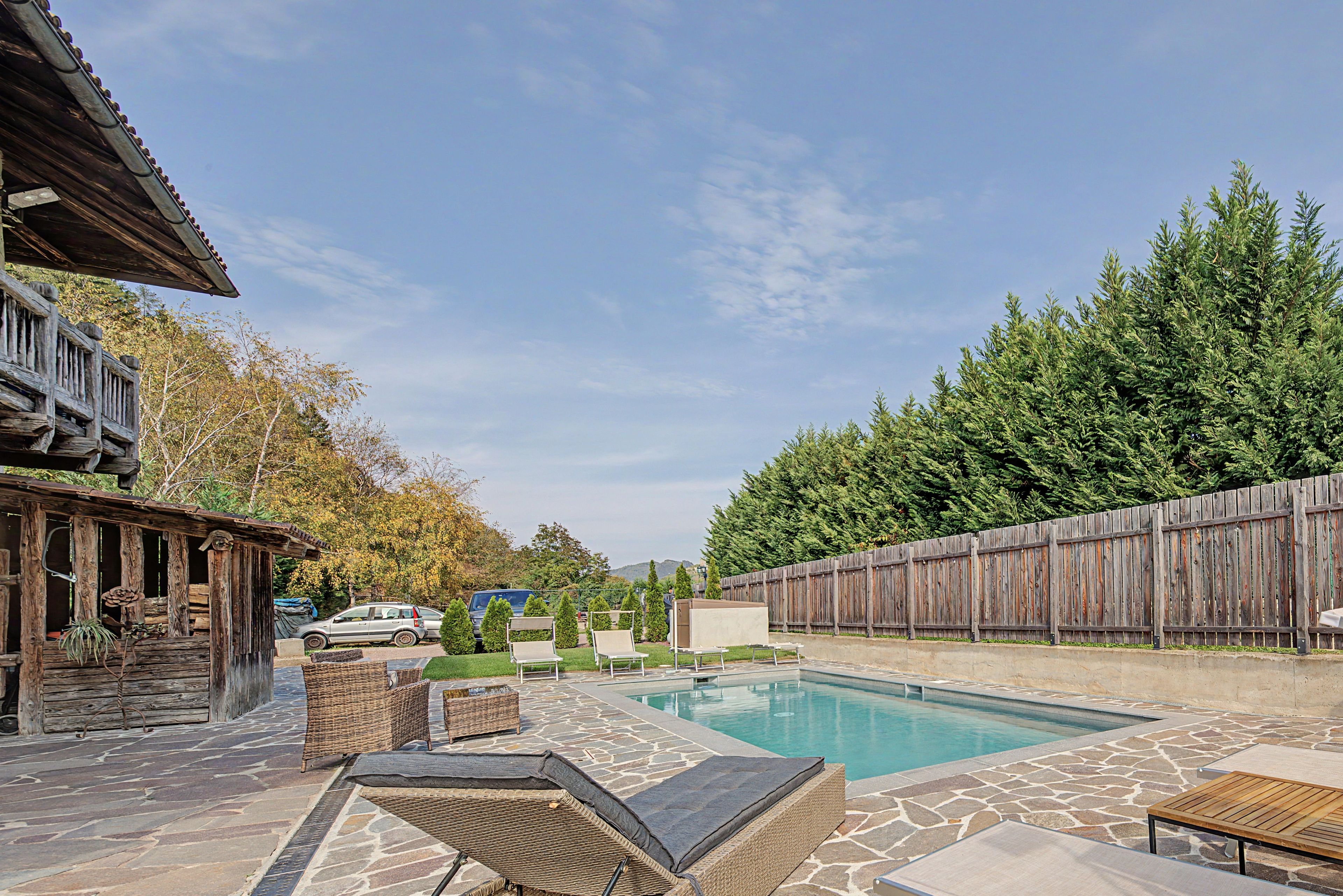 A backyard with a swimming pool, wicker furniture, and a wooden fence.