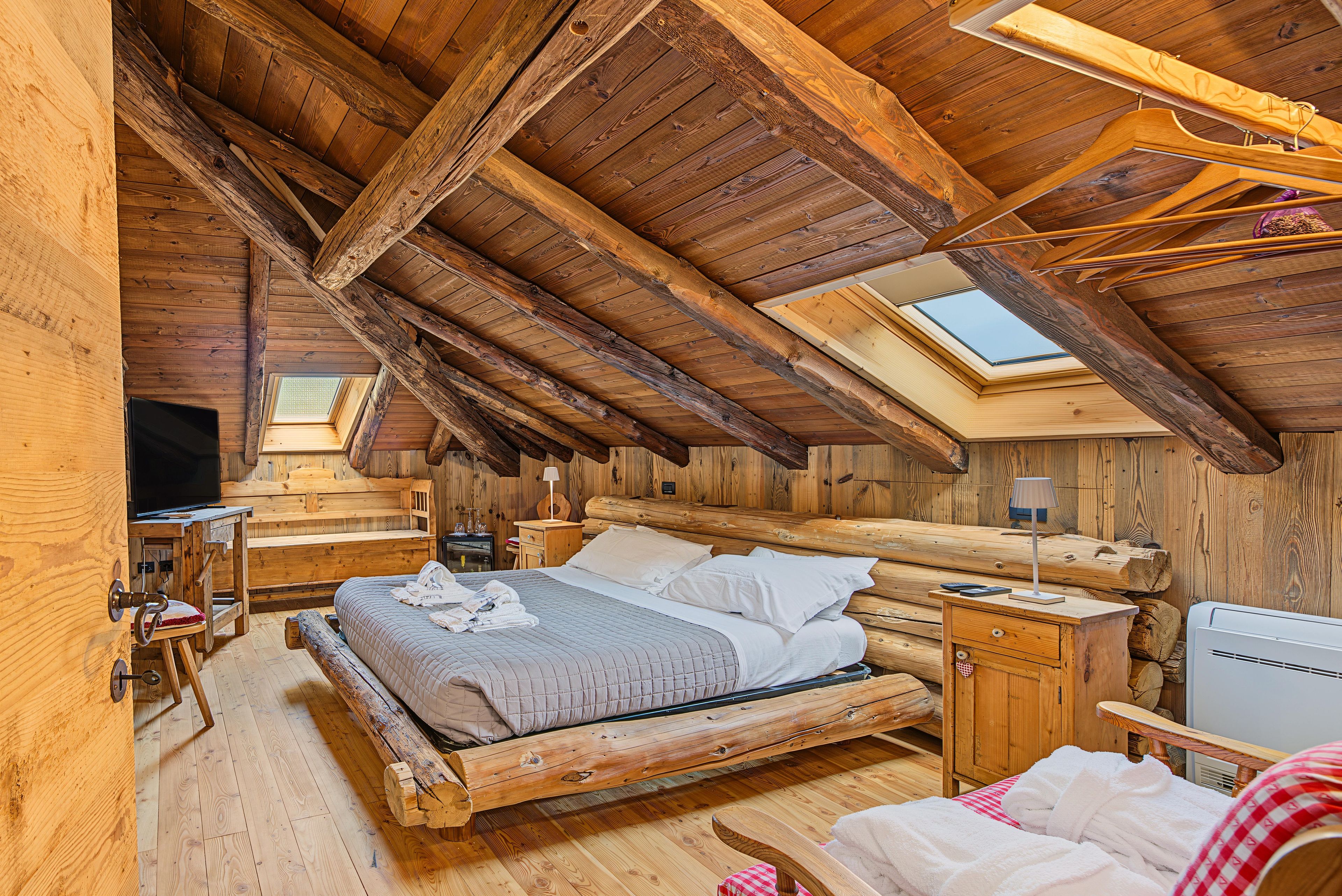 Une pièce rustique en bois, avec un plafond en pente, un lit, une table de chevet, une lampe et une fenêtre.