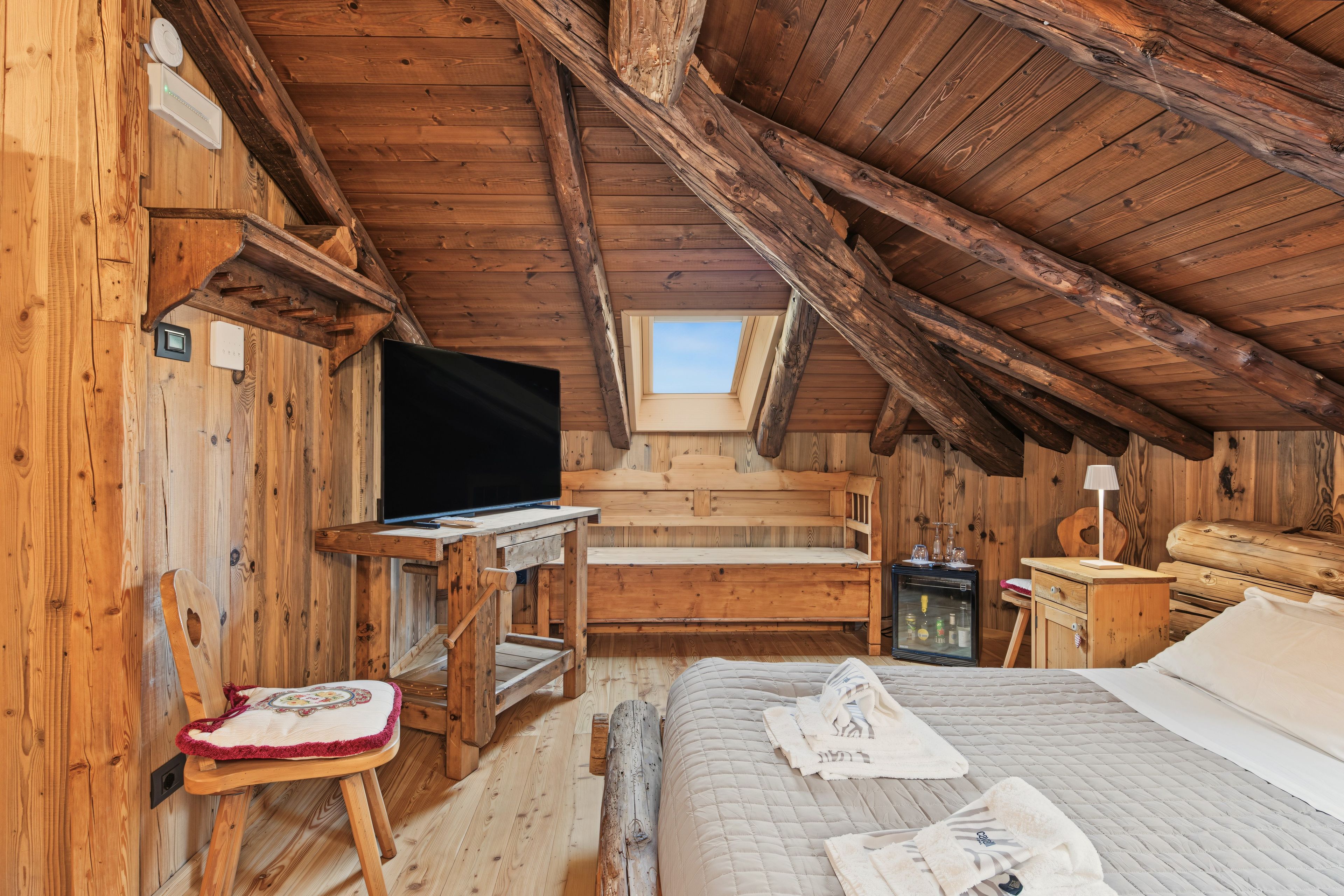 A cozy attic room with wooden walls, a bed, a desk, and a television.