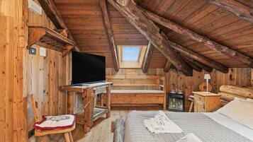 A cozy attic room with wooden walls, a bed, a desk, and a television.