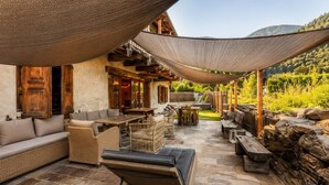 Een terras buiten met stenen vloer, rieten meubels en een houten pergola voor beschutting.