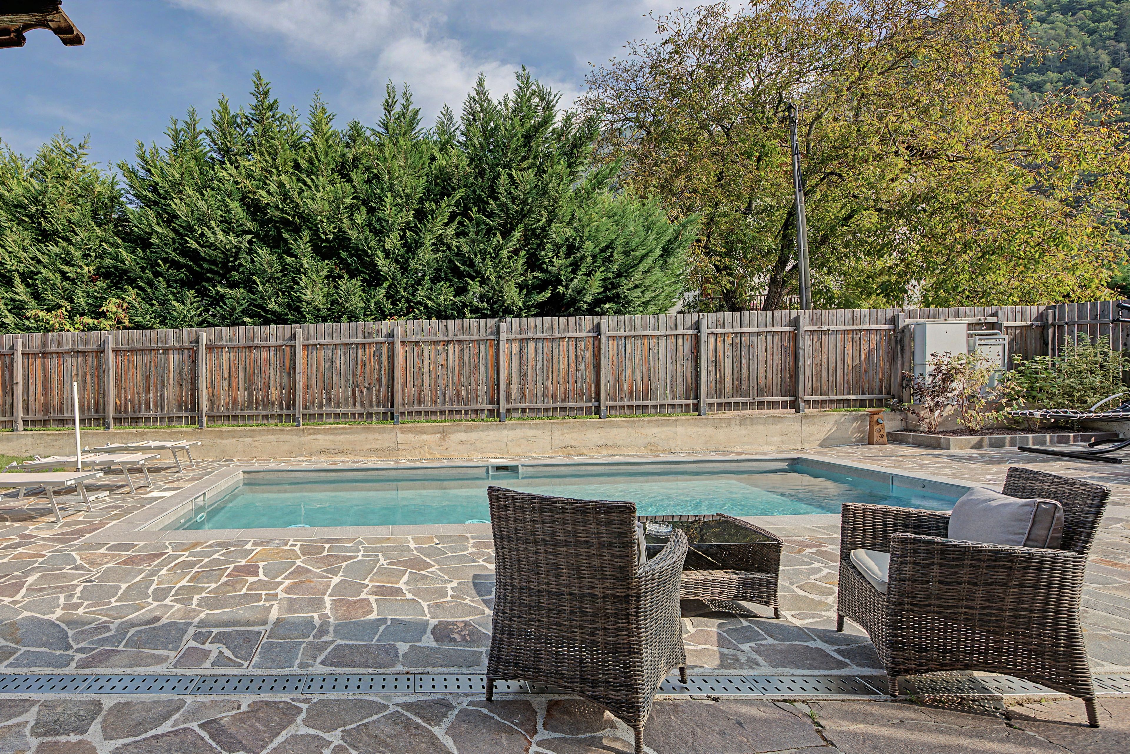 A swimming pool with stone flooring and wicker furniture.