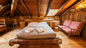 Een houten chalet met een slaapkamer op entresol, met een bed, een rood-wit geblokte bank, een houten bureau en een kleine stoel.