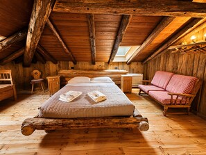 Eine Holzhütte mit Schlafzimmer auf dem Dachboden, ausgestattet mit einem Bett, einem rot-weiß karierten Sofa, einem Holztisch und einem kleinen Stuhl.