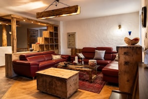 A cozy living room with a red leather sofa, a wooden coffee table, and a rustic wooden cabinet.
