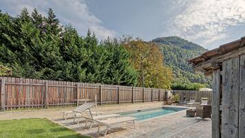 A backyard with a swimming pool, lounge chairs, and a wooden fence.