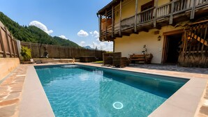 Una piscina rettangolare con bordatura in pietra, un solarium in legno e una recinzione di legno.