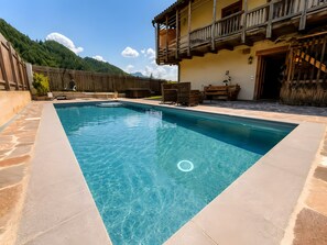 Ein rechteckiger Swimmingpool mit Steinrand, Holzterrasse und Holzzaun.