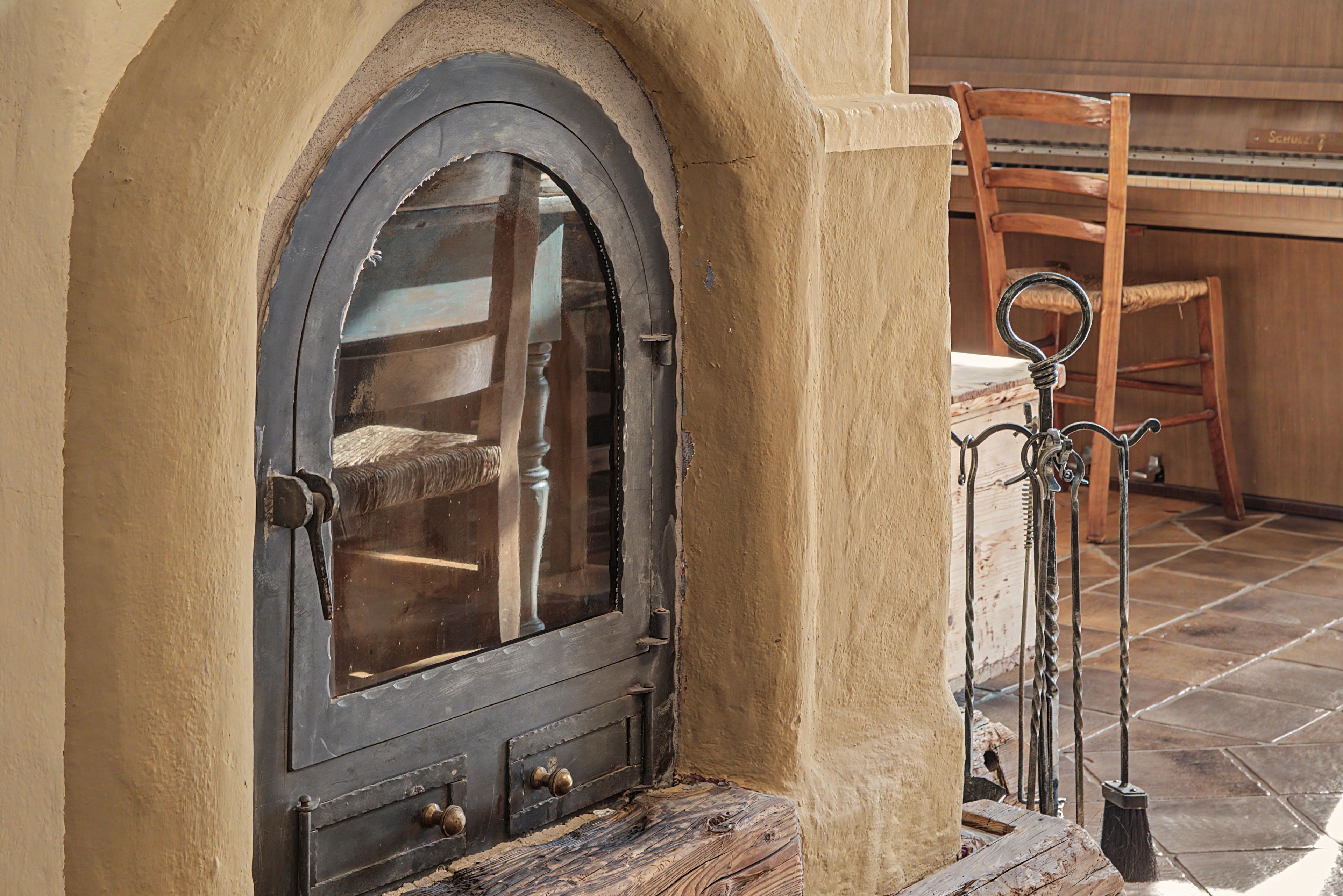 Eine rustikale Holztür mit Metallbeschlag und kleinem Fenster, in eine beige Wand mit Steinboden eingelassen.