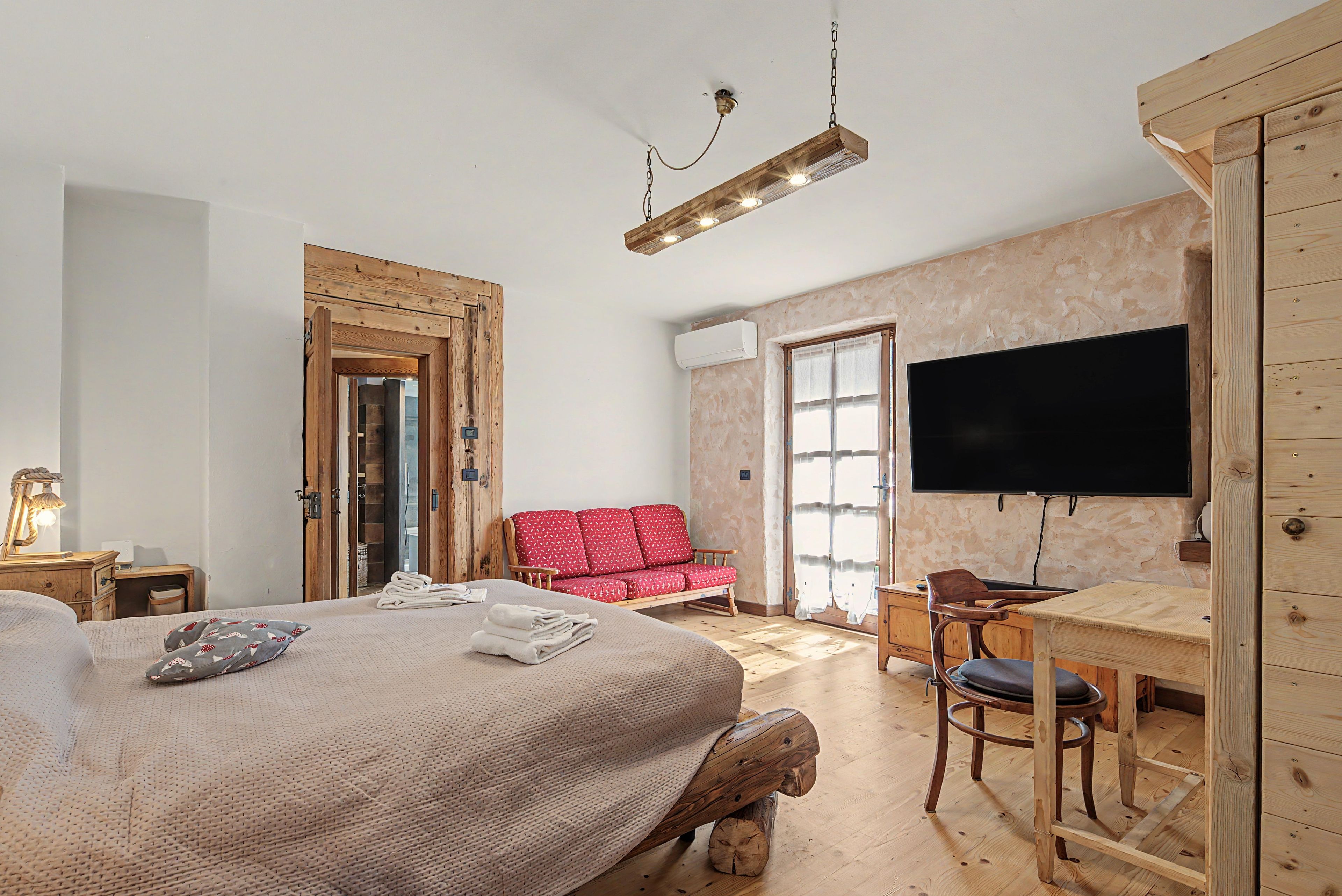 Ein Schlafzimmer mit einem Bett, einem roten Sofa, einem Holztisch, einem Fernseher und einer hölzernen Deckenleuchte.