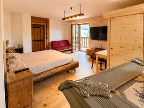 Ein Zimmer mit Holzboden, einem Bett, einem roten Sofa, einem Schreibtisch und einem Fernseher.