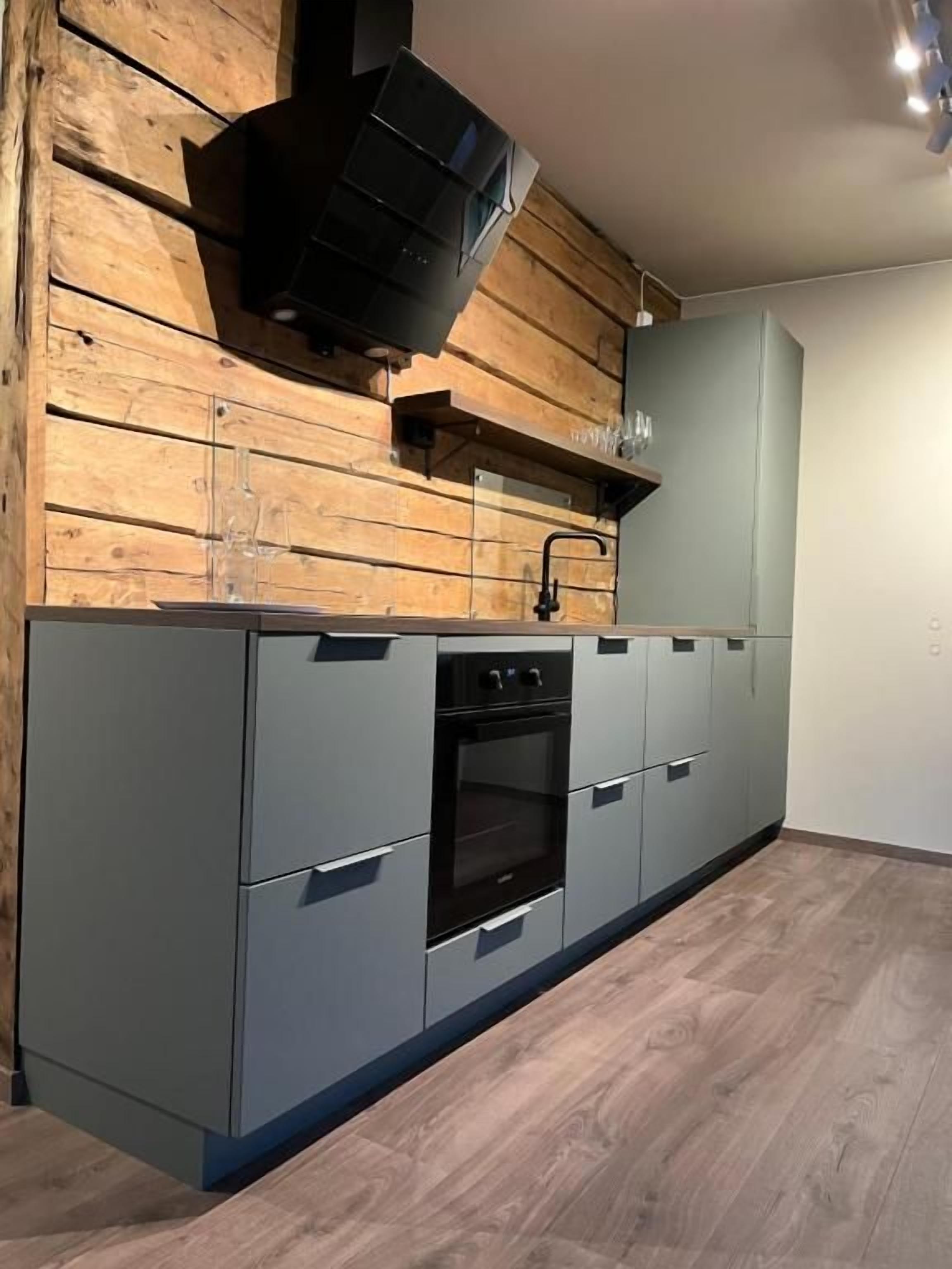 Una cocina con horno empotrado, microondas y un panel de pared de madera.