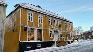 A yellow building with a staircase leading to the entrance, a visible shop window, and a snow-covered street. - Historic Strandgata 36 (Troms)