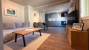 A modern living room with a sofa, coffee table, and chairs. There is a kitchen in the background with cabinets and a TV. - Historic Strandgata 36 (Troms)