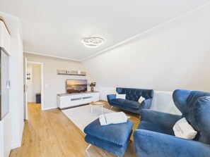 Uma sala de estar moderna com televisão de tela plana, sofá azul e piso de madeira.