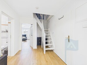 Ein Flur mit Holzboden, weißen Wänden, einer weißen Treppe und einer Tür mit Messingklinke.