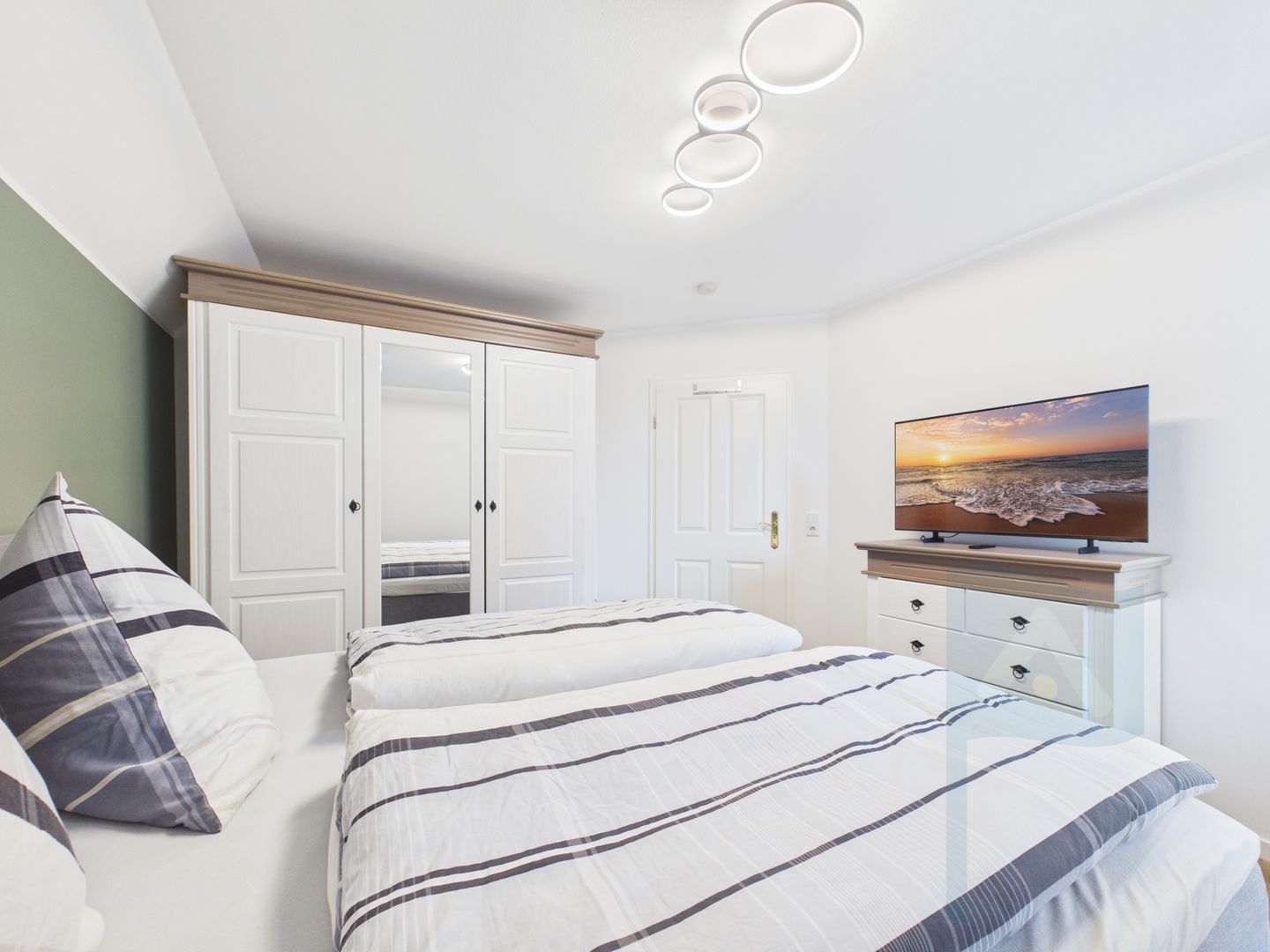 Une chambre à coucher avec un lit, une armoire, un téléviseur posé sur un meuble et un tableau accroché au mur.