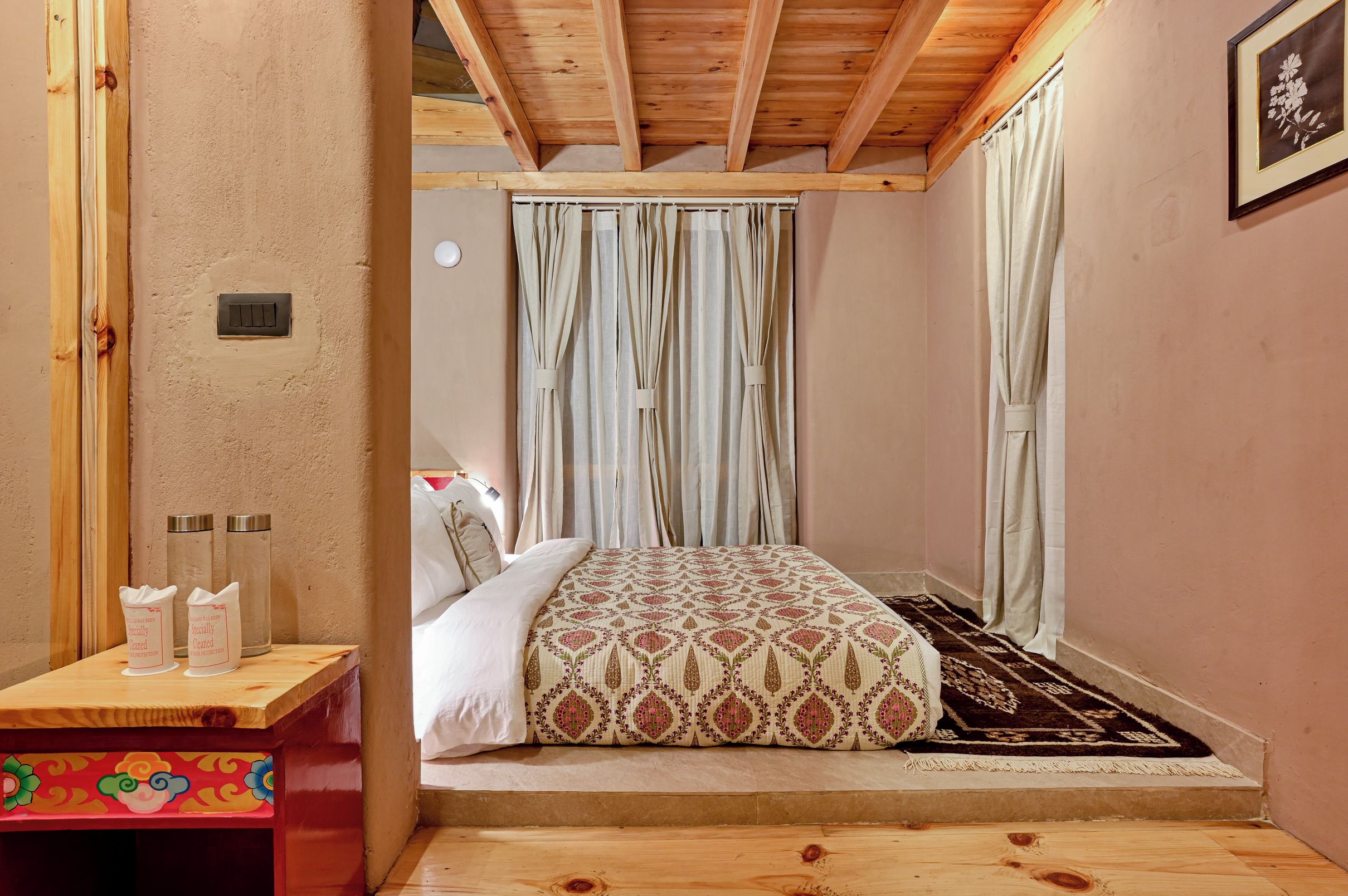 Quarto com cama, cortinas, mesa de cabeceira com dispensador de lenços e um tapete pequeno.