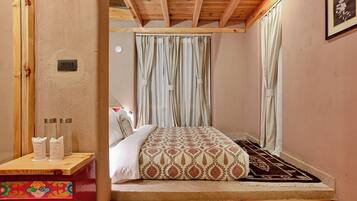 Quarto com cama, cortinas, mesa de cabeceira com dispensador de lenços e um tapete pequeno.