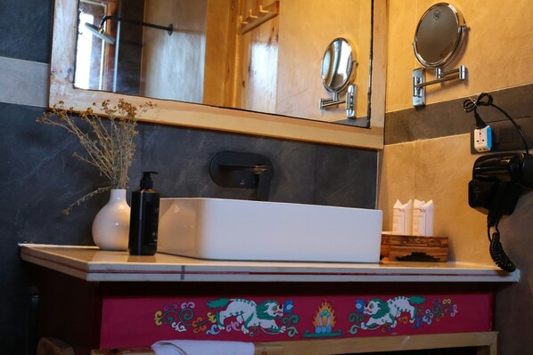 Un baño con un lavamanos blanco, un espejo, un teléfono y un mueble decorativo con un diseño floral rojo.