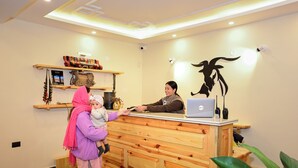 En receptionsdisk med en bærbar computer, en dekorativ vægdekoration og en reol med genstande.