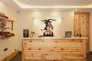A reception desk with a wooden finish, a laptop, and a wall-mounted sign indicating an office. - Changpa Lodge (Leh)