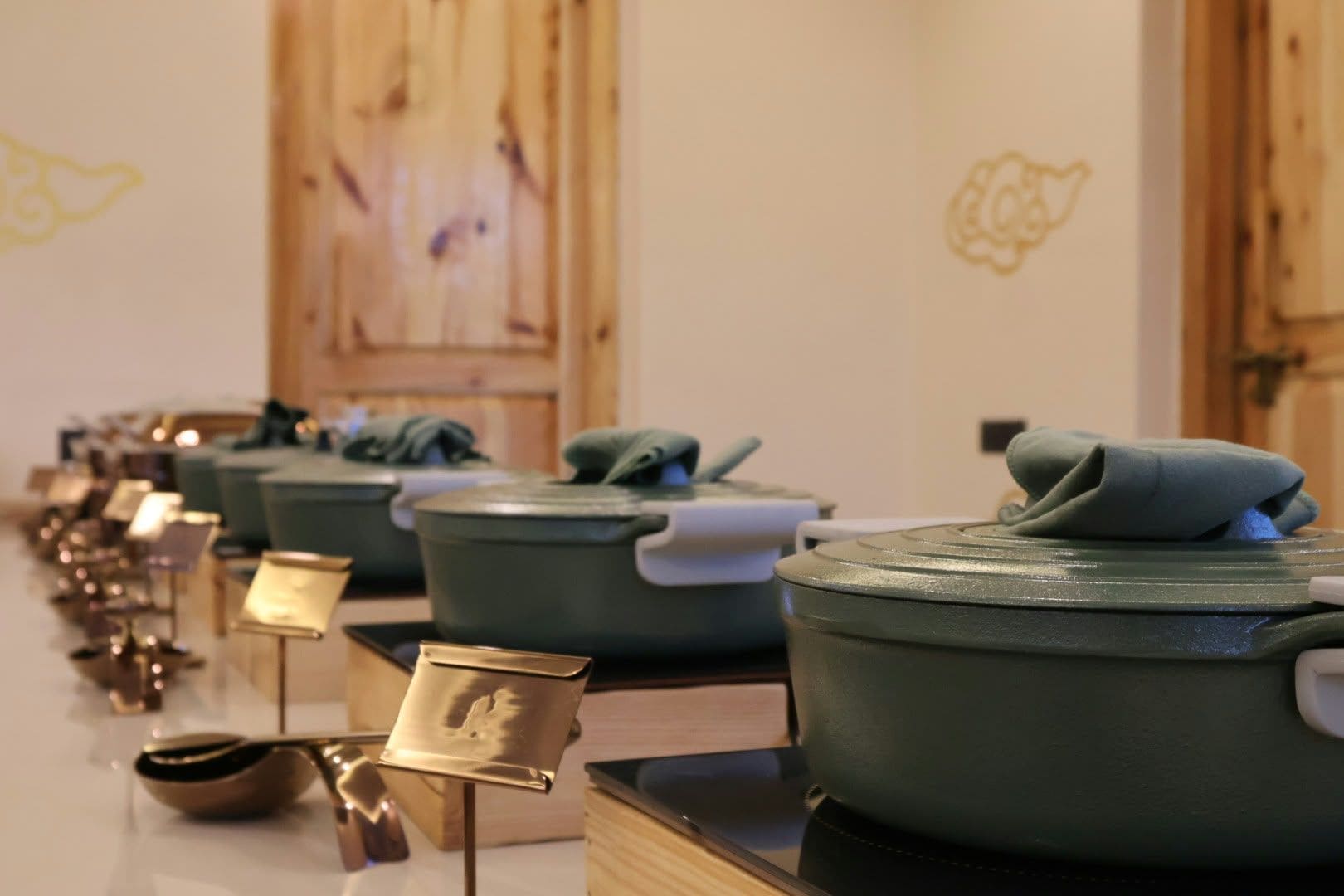 A row of kitchenware on display, including pots and a teapot, with a wooden backdrop and wall art.