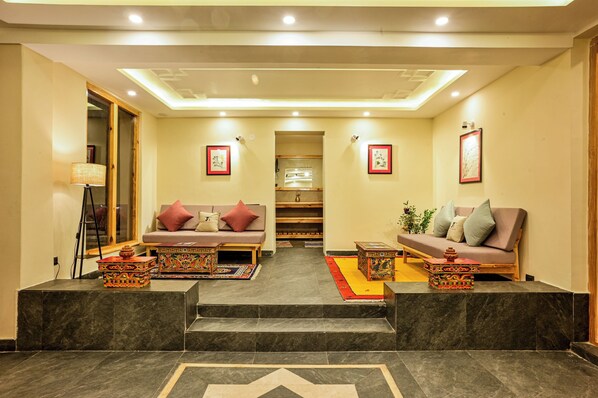 A hotel lobby with two sofas facing each other, a staircase leading to a second floor, and a reception desk. - Changpa Lodge (Leh)