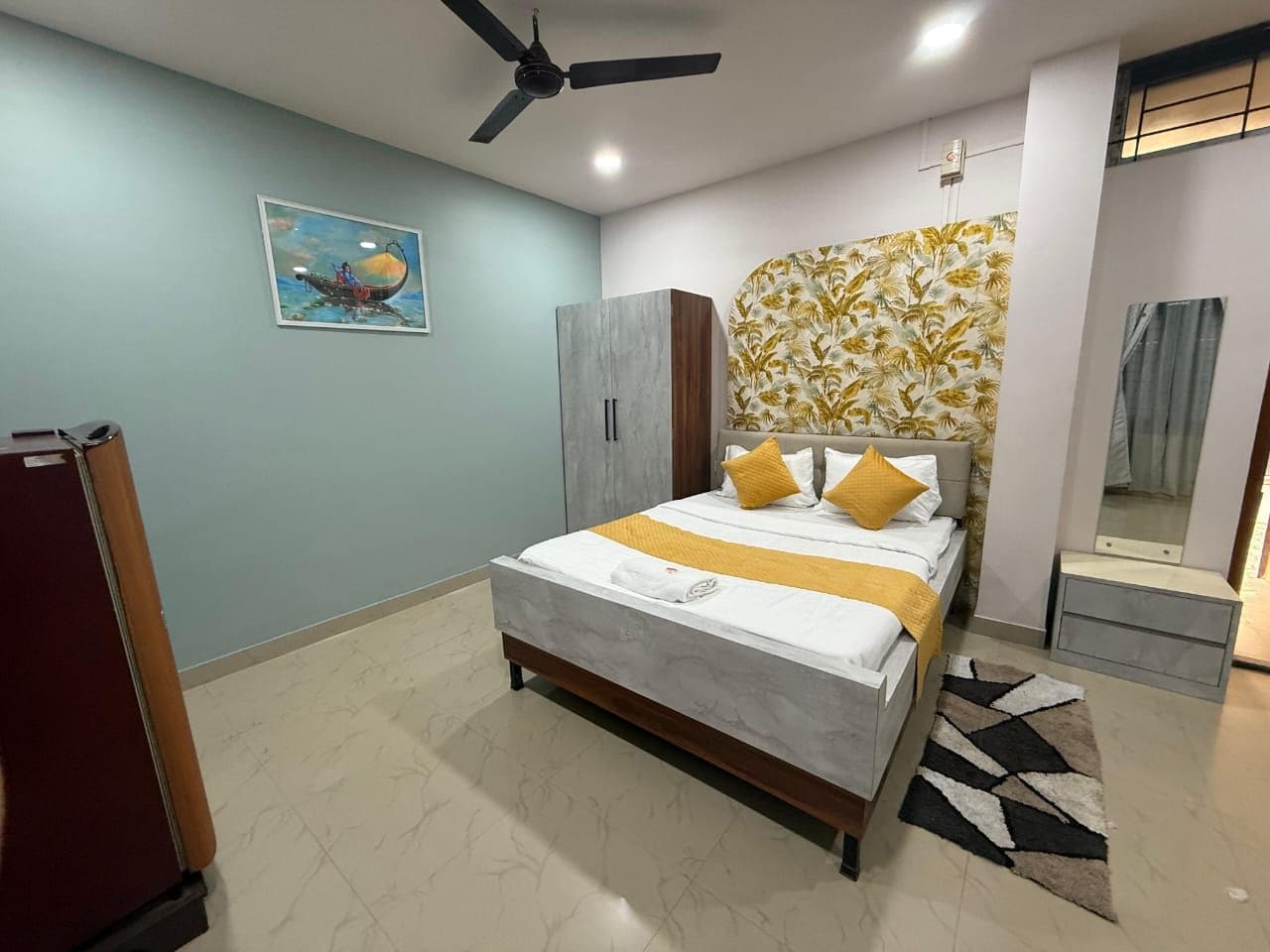 Quarto com cama, ventoinha no teto, guarda-roupa, espelho e um quadro na parede.