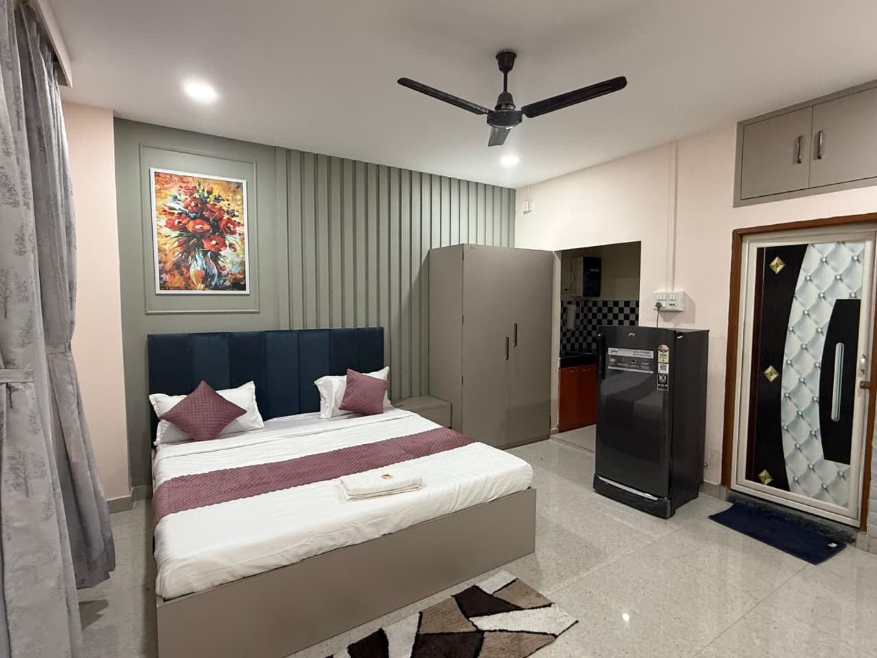Quarto de hotel com cama, ventoinha no teto, frigorífico e guarda-roupa.