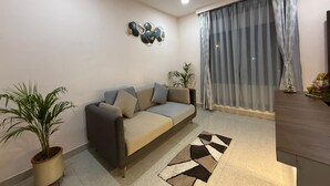 A living room with a sofa, a ceiling fan, a large window with curtains, and a decorative wall piece. - Atithi Guest House  (Guwahati)