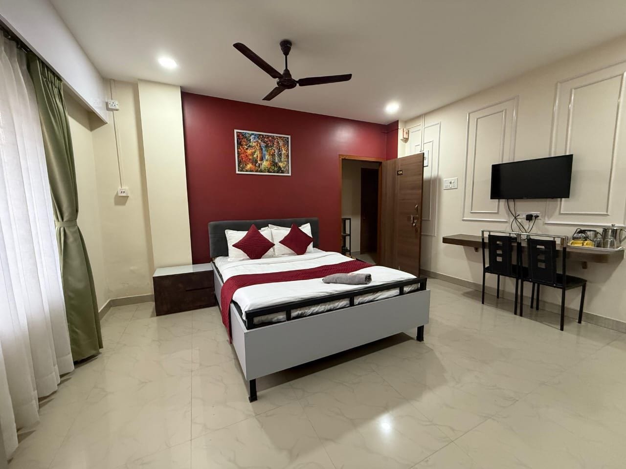 Quarto com cama, ventoinha no teto, televisão e escrivaninha com cadeiras.