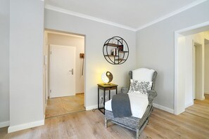 A room with a wicker chair, a small table with a lamp, and a wall-mounted shelf. - La Maison Eichenweg App 1 + 3 - Townhouse on Eichenweg (Scharbeutz)