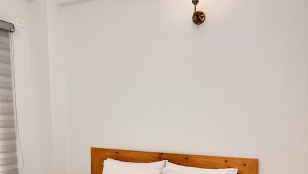 Een net opgemaakt bed met witte lakens en een opgevouwen handdoek, een houten hoofdbord, nachtkastjes en een wandlamp.