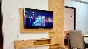 Een moderne hotelkamer met een flatscreen-televisie bevestigd aan een wand van houtpanelen, een tafel met marmeren blad en een doosje zakdoekjes, en een houten vloer.