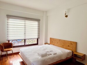 Una camera da letto con un letto, una sedia, un comodino e una finestra con persiane.
