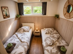 Habitación compacta con dos camas, una ventana con cortinas, una mesita de noche con lámpara y un espejo instalado en la pared.