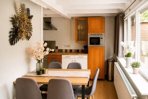 A compact kitchen with a dining area, wooden cabinets, a microwave, and a window with a view. - Zenda's natuurhuisje (Lanaken)