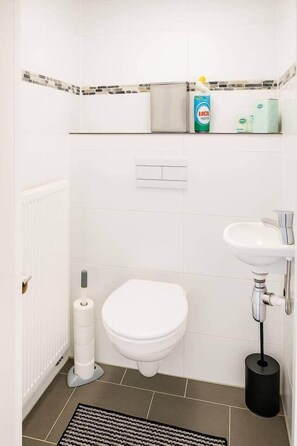 Een badkamer met een toilet, een wastafel, een toiletpapierhouder en een rol toiletpapier.