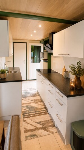 A modern kitchen with white cabinets, a black countertop, and a patterned rug. - Zenda's vakantiehuisje (Lanaken)