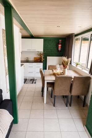 A dining area with a table set for four, a kitchen in the background, and a fire extinguisher mounted on the wall. - Zenda's vakantiehuisje (Lanaken)