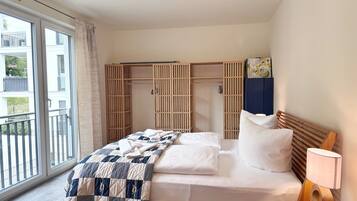 A bedroom with a bed, bedside table, lamp, and a wardrobe with a view to the outside.