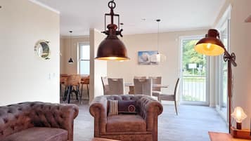 A spacious living room with a brown leather sofa, a round coffee table, and a dining area with a table and chairs.