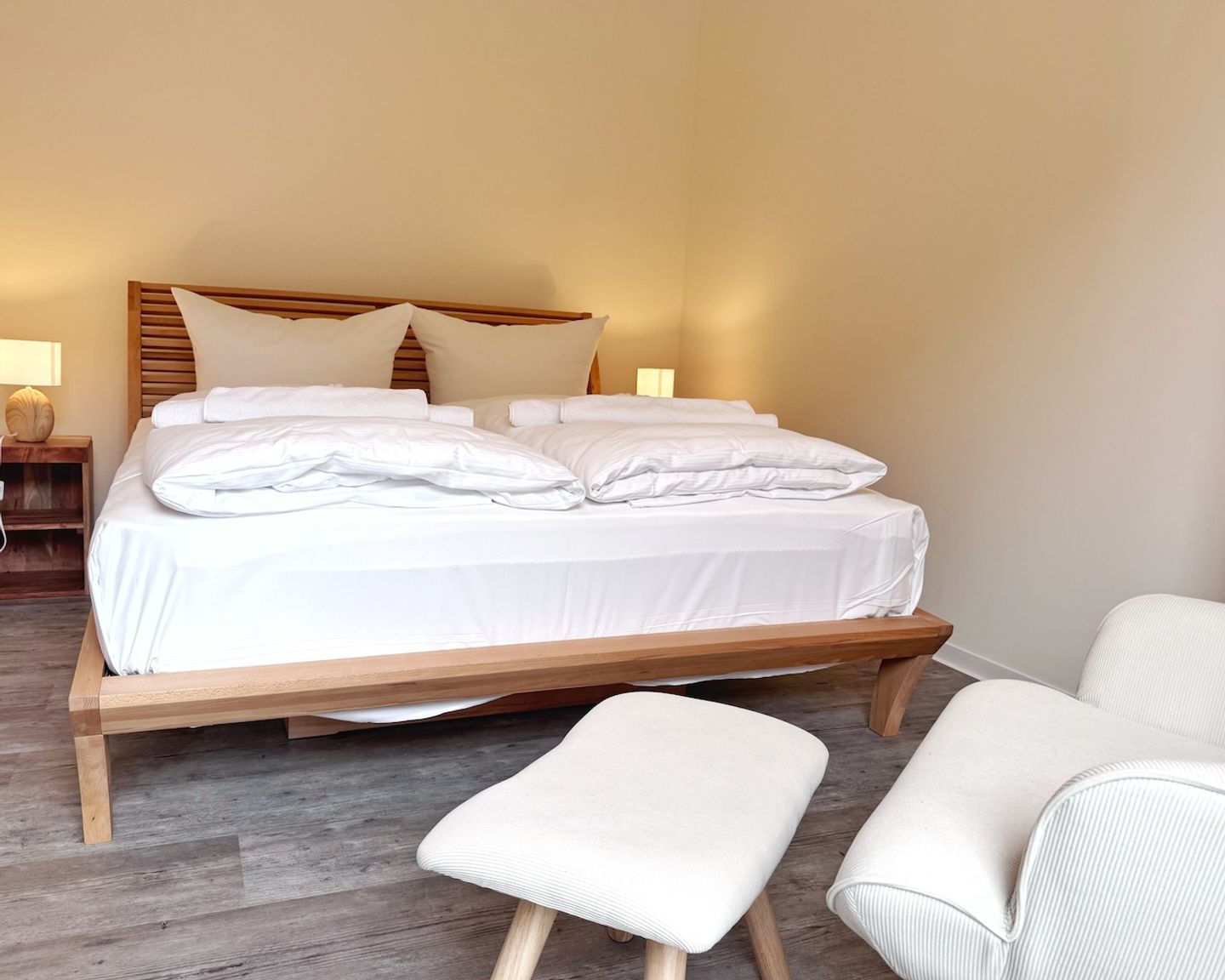 A neatly made bed with white linens and pillows, a wooden headboard, and a bedside table with a lamp.