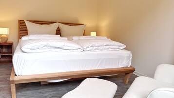 A neatly made bed with white linens and pillows, a wooden headboard, and a bedside table with a lamp.