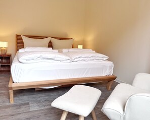 A neatly made bed with white linens and pillows, a wooden headboard, and a bedside table with a lamp. - Kogge 6 Apartment - Kogge Vacation Rental (Sassnitz)