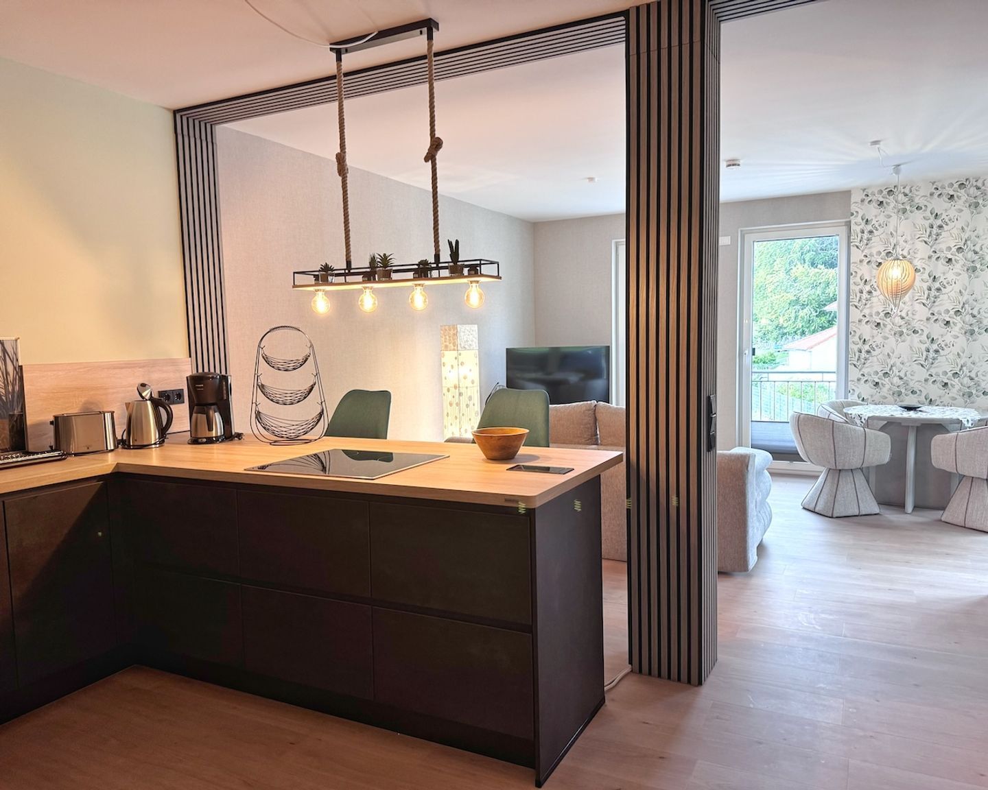 Eine moderne Küche mit Kochinsel, ein Essbereich mit rundem Tisch und ein Wohnzimmer mit Sofa und Fernseher.