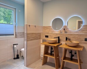 Ein modernes Badezimmer mit zwei hölzernen Waschtischen, einem großen Spiegel und einem Fenster mit Jalousien.