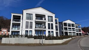 Um edifício residencial moderno de vários andares, com varandas, calçada pavimentada e céu azul claro.